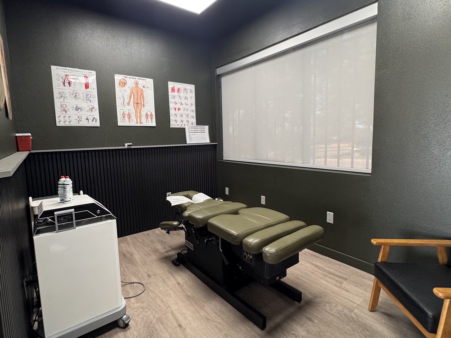 A treatment room at WLF Club with an adjustment table, anatomy charts, and a therapy cart.
