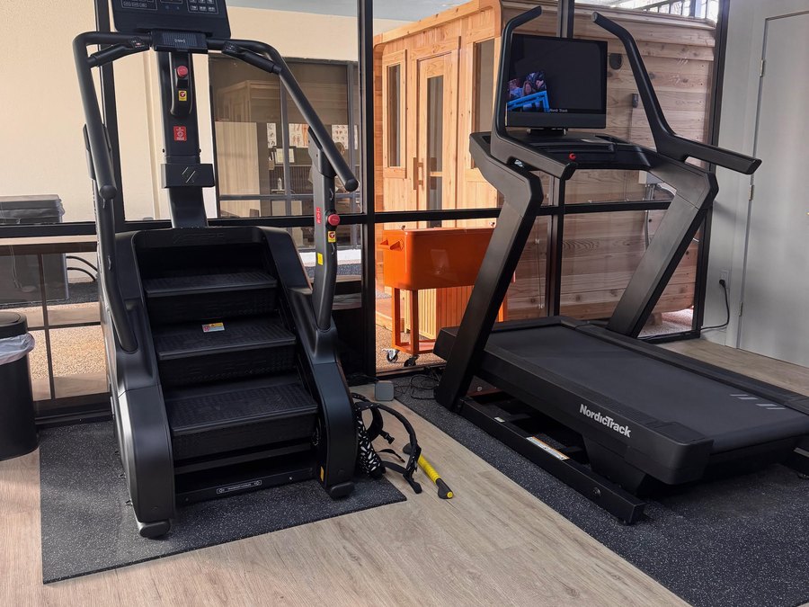 A STEPR stair climber and a treadmill facing floor-to-ceiling windows at WLF Club.