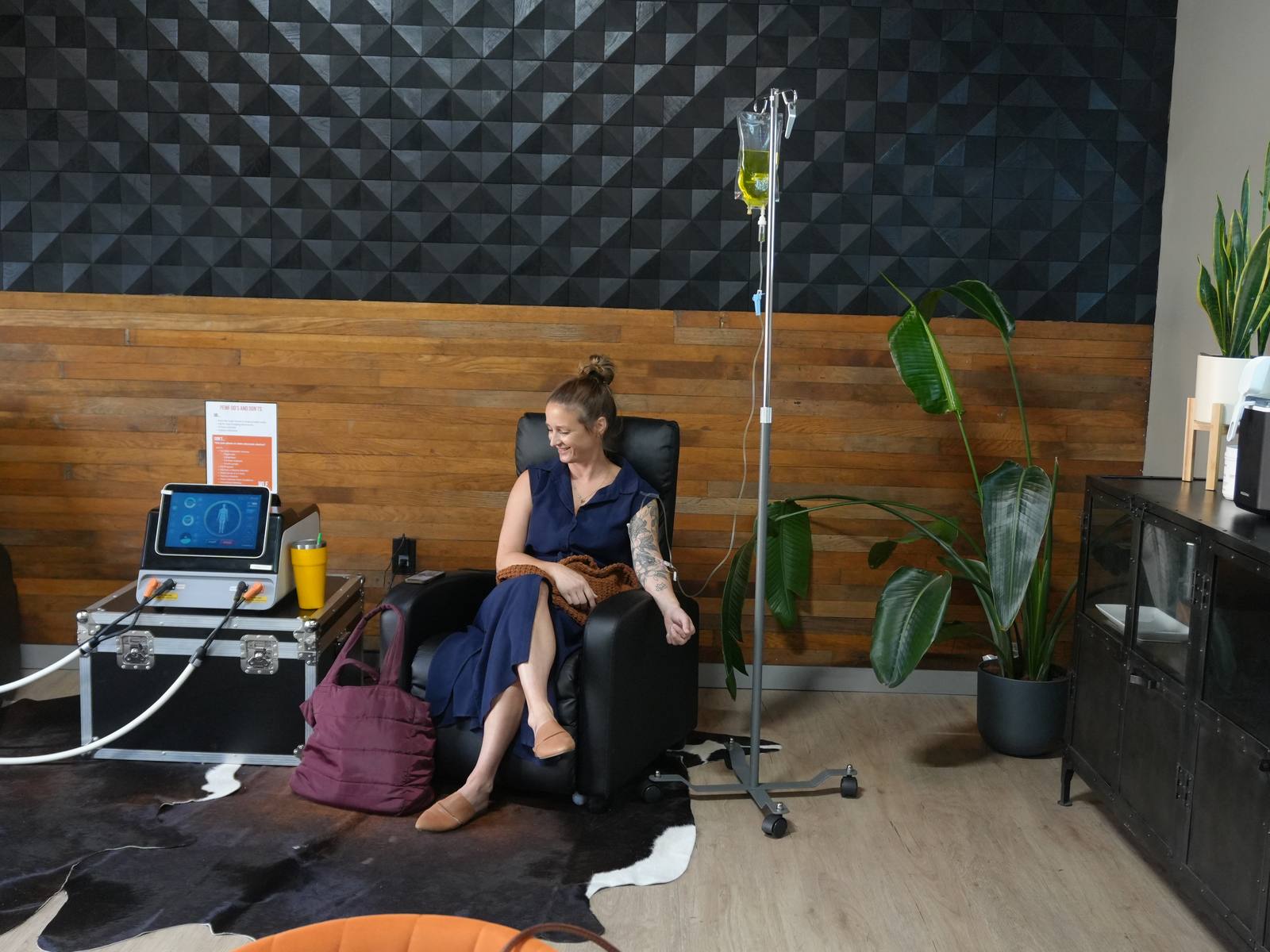 A member seated in a black recliner in the WLF recovery lounge with an infusion running from a bag on a rolling IV stand.