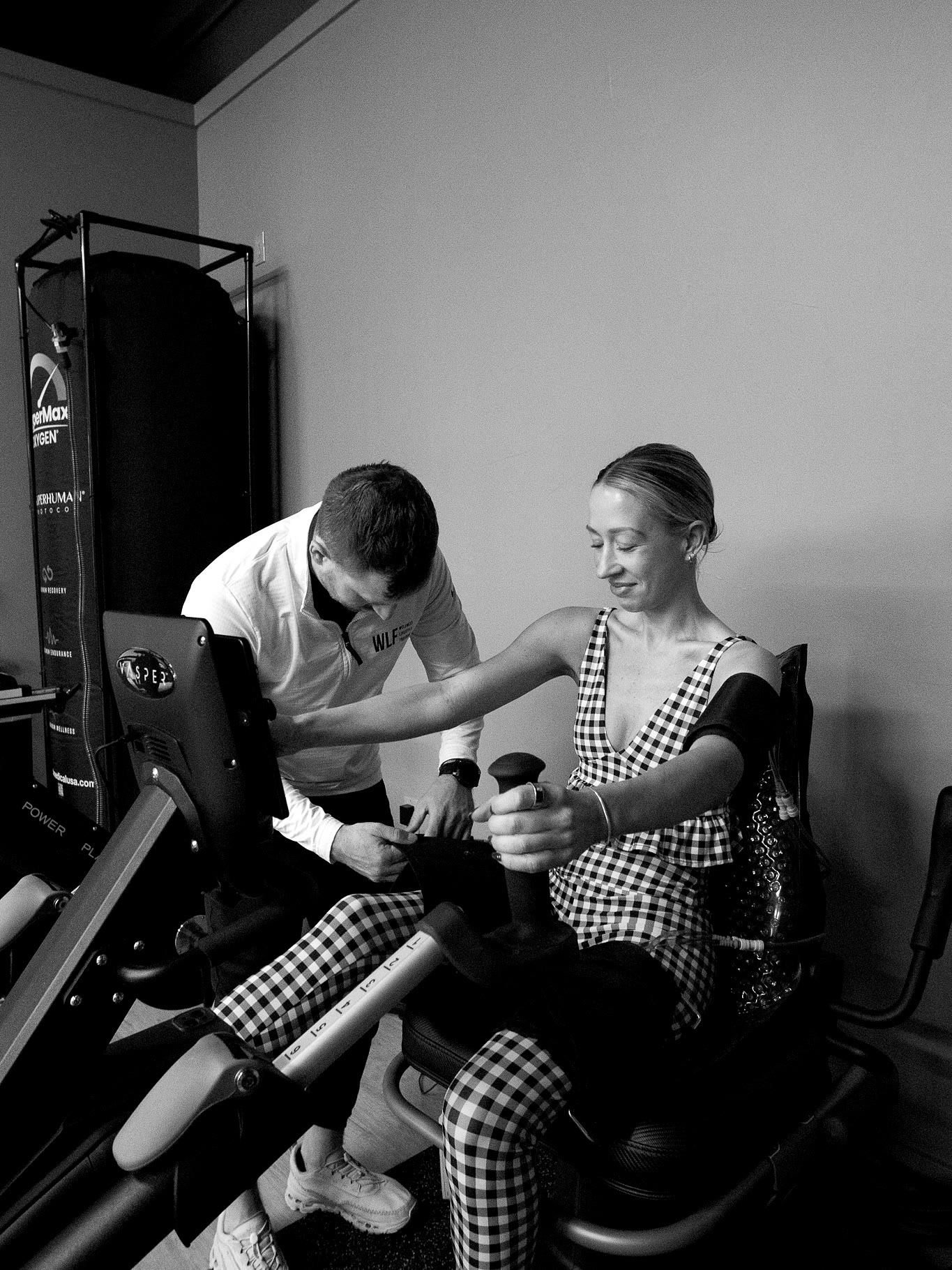 A WLF trainer setting a member up on the Vasper machine, shot in black and white.