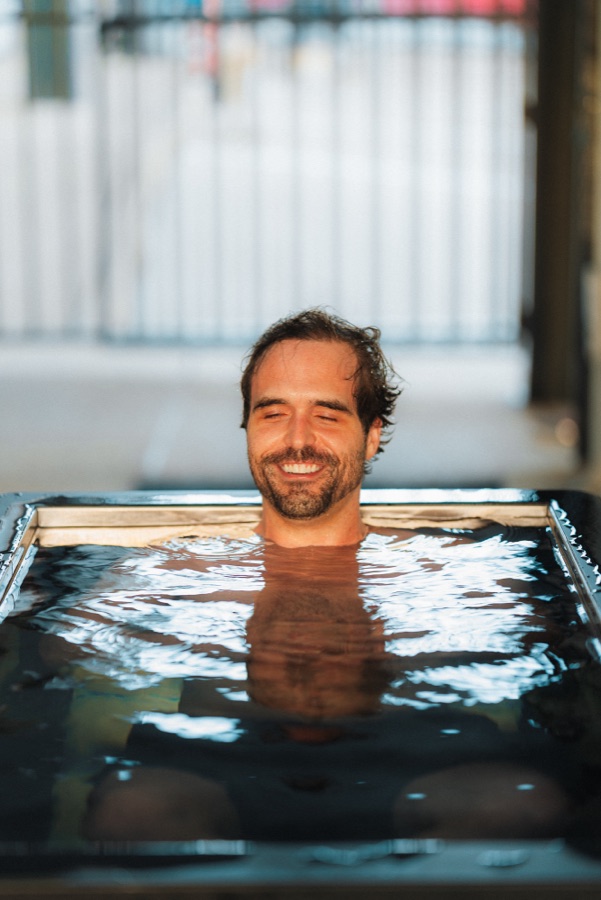 A WLF member submerged to the neck in the cold plunge, eyes closed and smiling.